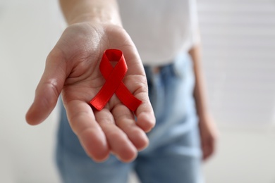 Woman holding red awareness ribbon on light background, closeup with space for text. World AIDS disease day Photo of Woman holding red awareness ribbon on light background, closeup with space for text. World AIDS disease day