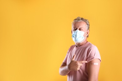 Senior man in protective mask pointing at arm with bandage after vaccination on yellow background. Space for text Photo of Senior man in protective mask pointing at arm with bandage after vaccination on yellow background. Space for text