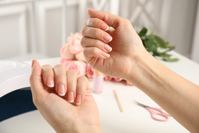 Woman doing manicure with ultraviolet nail lamp at white table, closeup Photo of Woman doing manicure with ultraviolet nail lamp at white table, closeup