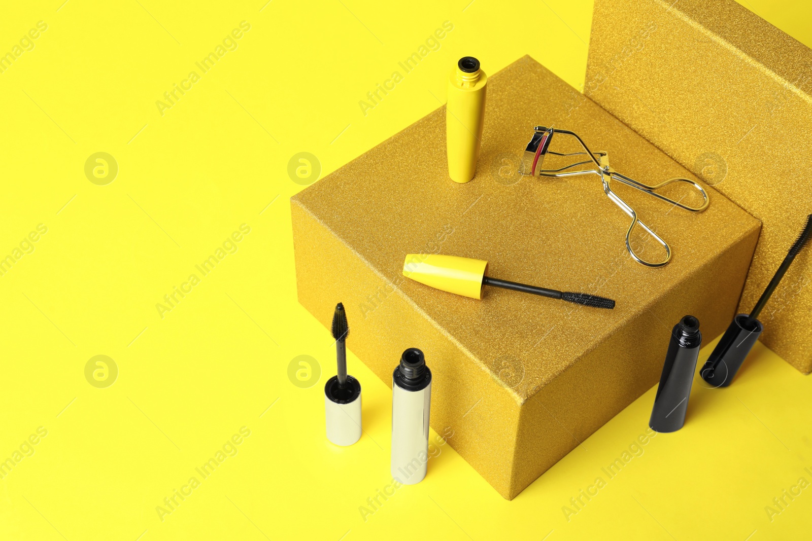Different mascaras and eyelash curler on yellow background. Makeup product Photo of Different mascaras and eyelash curler on yellow background. Makeup product