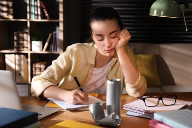 Tired young woman with energy drink studying at home Photo of Tired young woman with energy drink studying at home