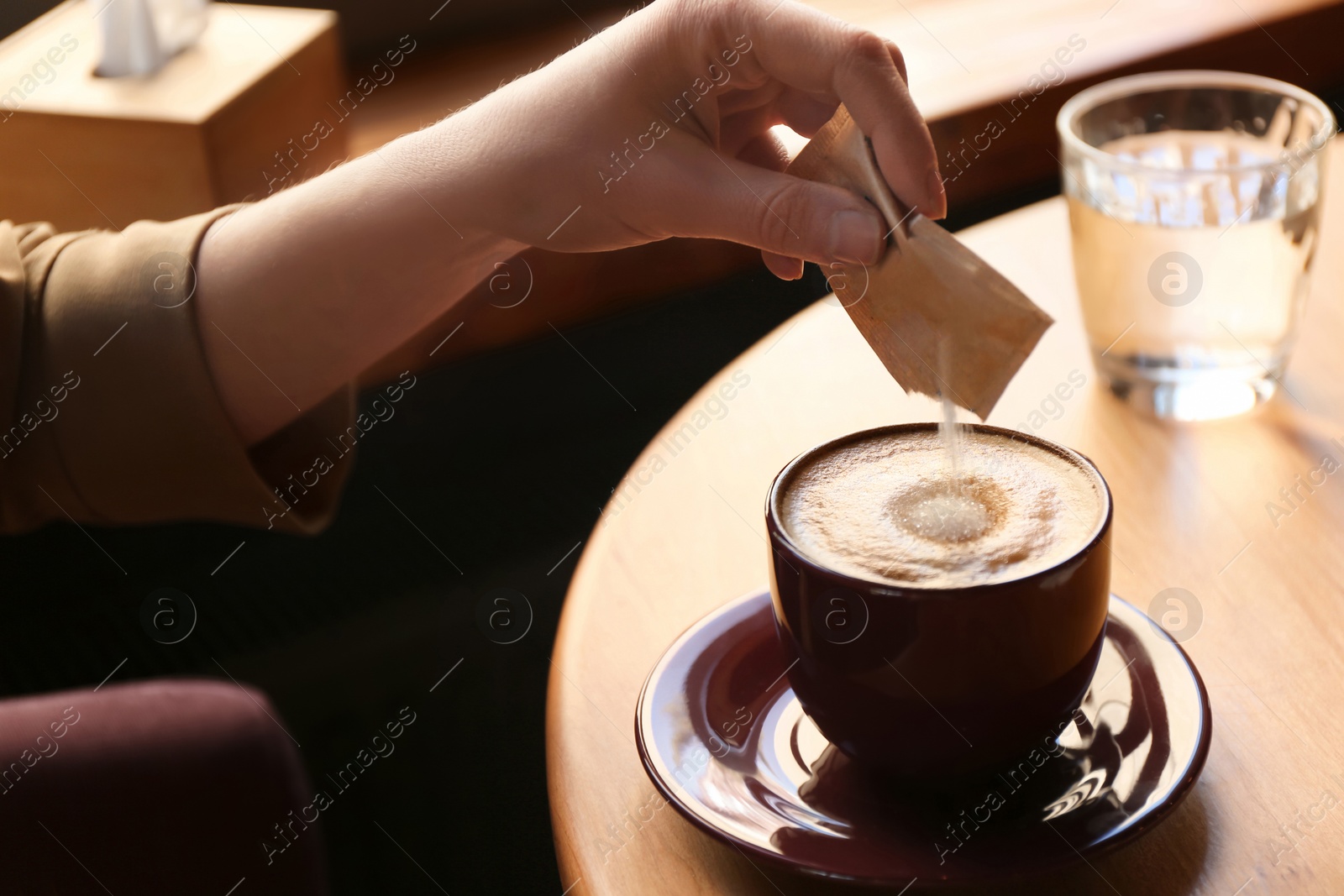Photo of Woman adding sugar to aromatic coffee at table in cafe, closeup