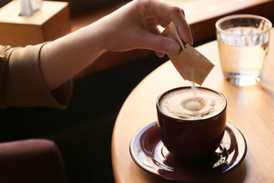 Photo of Woman adding sugar to aromatic coffee at table in cafe, closeup
