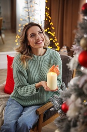 Young woman with candle near Christmas tree at home Photo of Young woman with candle near Christmas tree at home