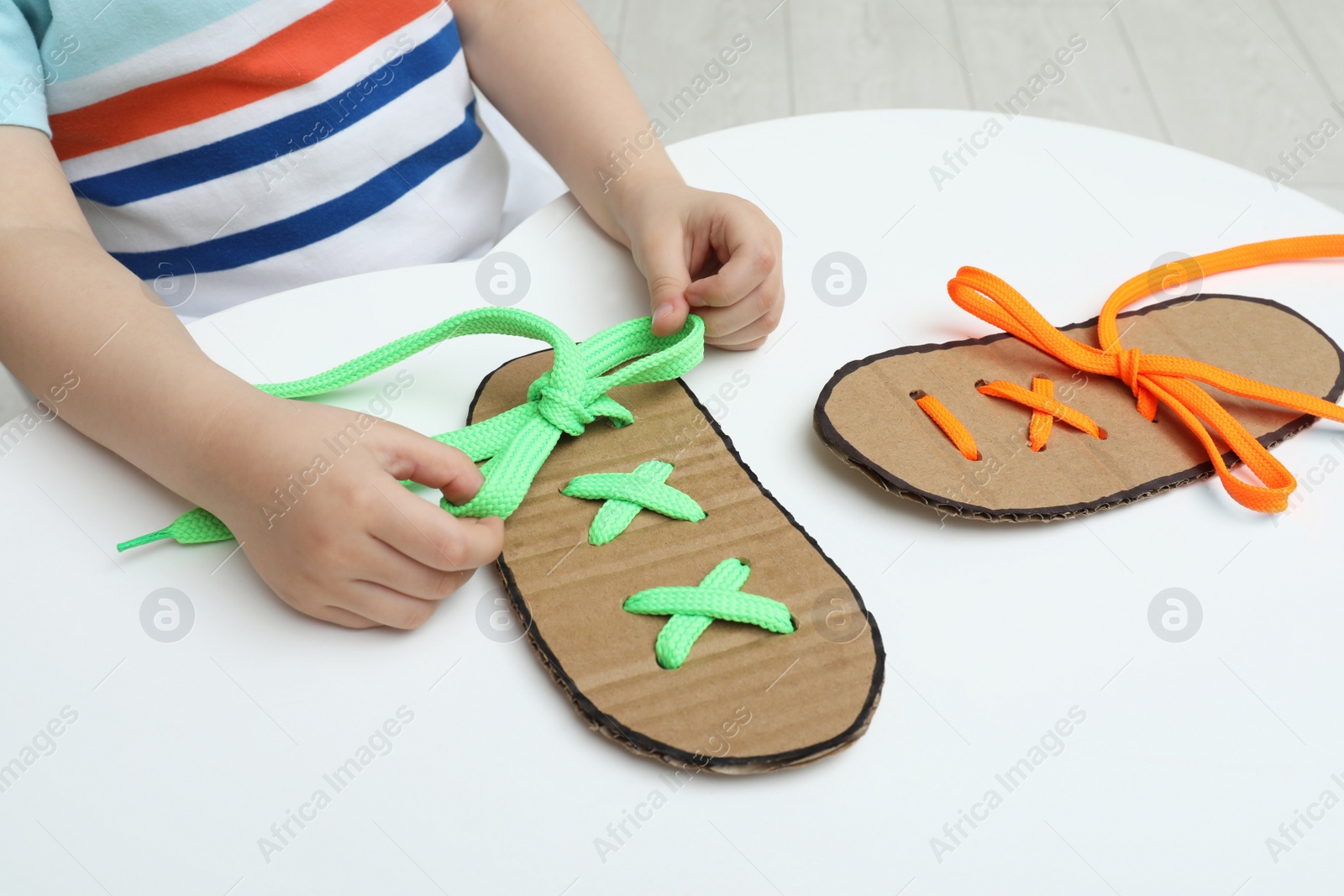 Little boy tying shoe lace using training cardboard template at white table, closeup Photo of Little boy tying shoe lace using training cardboard template at white table, closeup