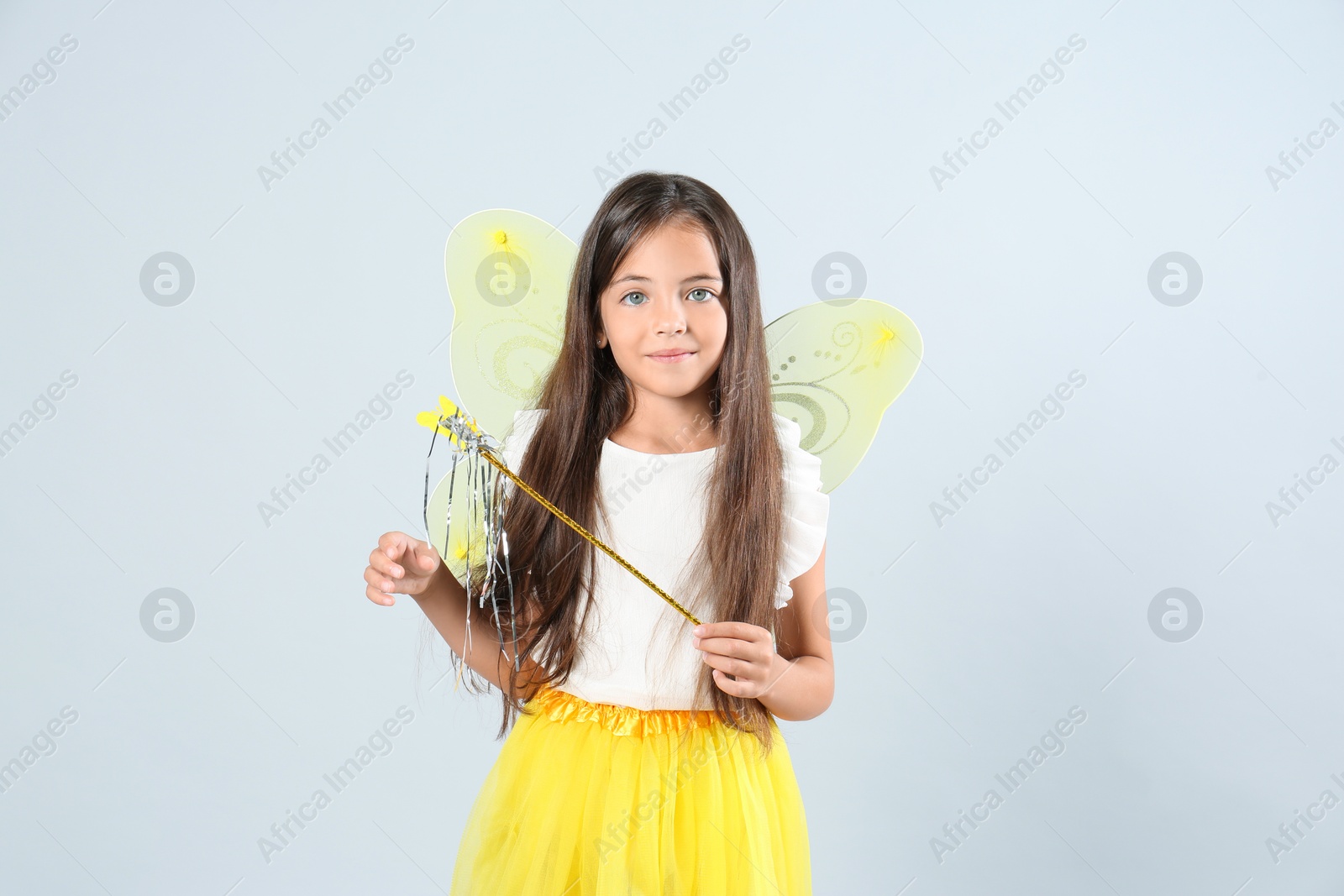 Cute little girl in fairy costume with yellow wings and magic wand on light background Photo of Cute little girl in fairy costume with yellow wings and magic wand on light background