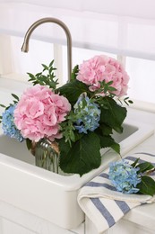 Vase with beautiful hortensia flowers in kitchen sink Photo of Vase with beautiful hortensia flowers in kitchen sink