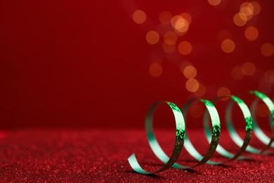 Shiny green serpentine streamer on red table against blurred lights, closeup. Space for text Photo of Shiny green serpentine streamer on red table against blurred lights, closeup. Space for text