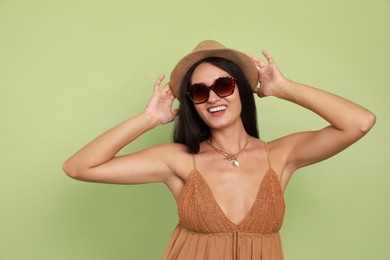Beautiful young woman with straw hat and stylish sunglasses on light green background Photo of Beautiful young woman with straw hat and stylish sunglasses on light green background