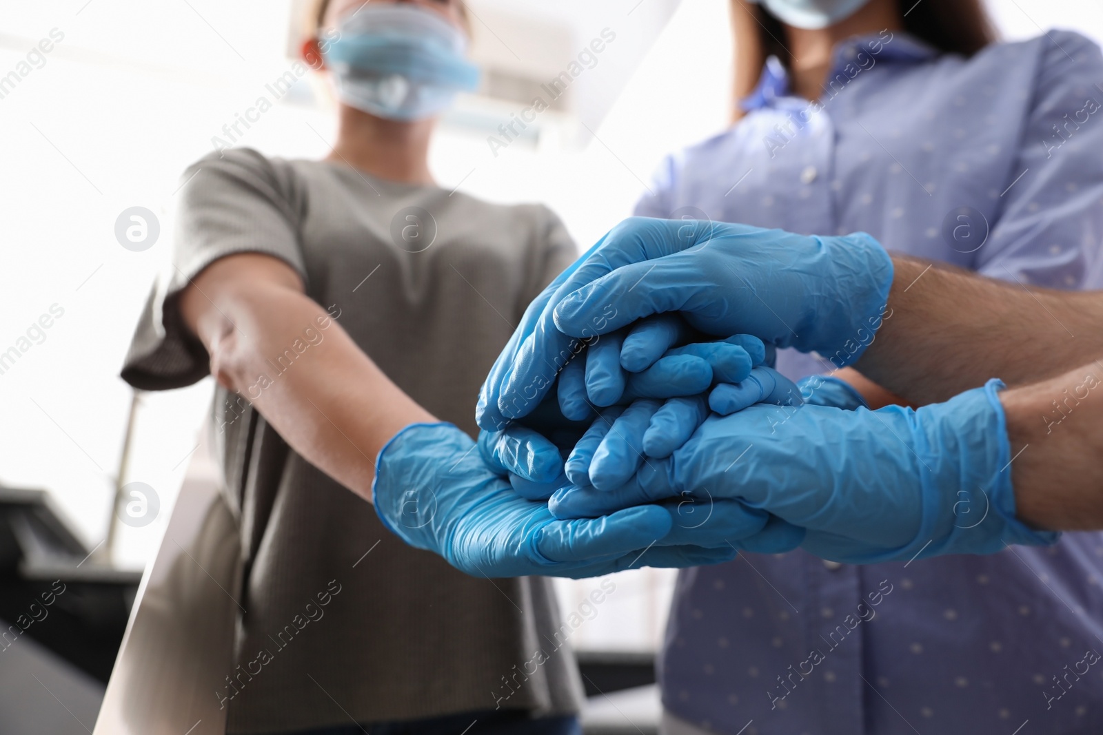 People in blue medical gloves stacking hands on blurred background, closeup Photo of People in blue medical gloves stacking hands on blurred background, closeup