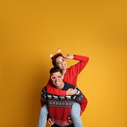 Couple in Christmas sweaters, Santa headband and party glasses on yellow background Photo of Couple in Christmas sweaters, Santa headband and party glasses on yellow background