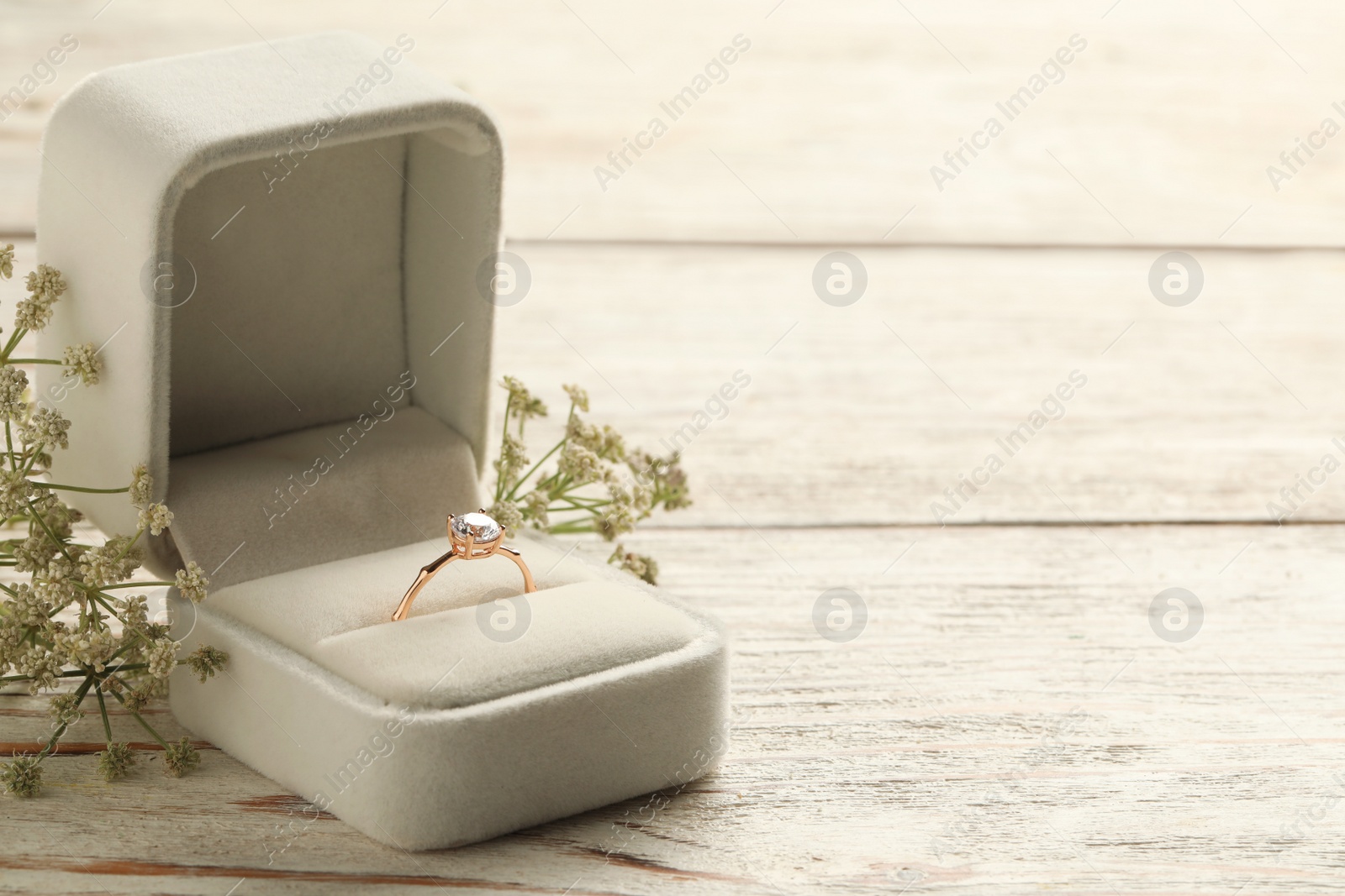 Beautiful engagement ring with gemstone in box and flowers on white wooden table. Space for text Photo of Beautiful engagement ring with gemstone in box and flowers on white wooden table. Space for text