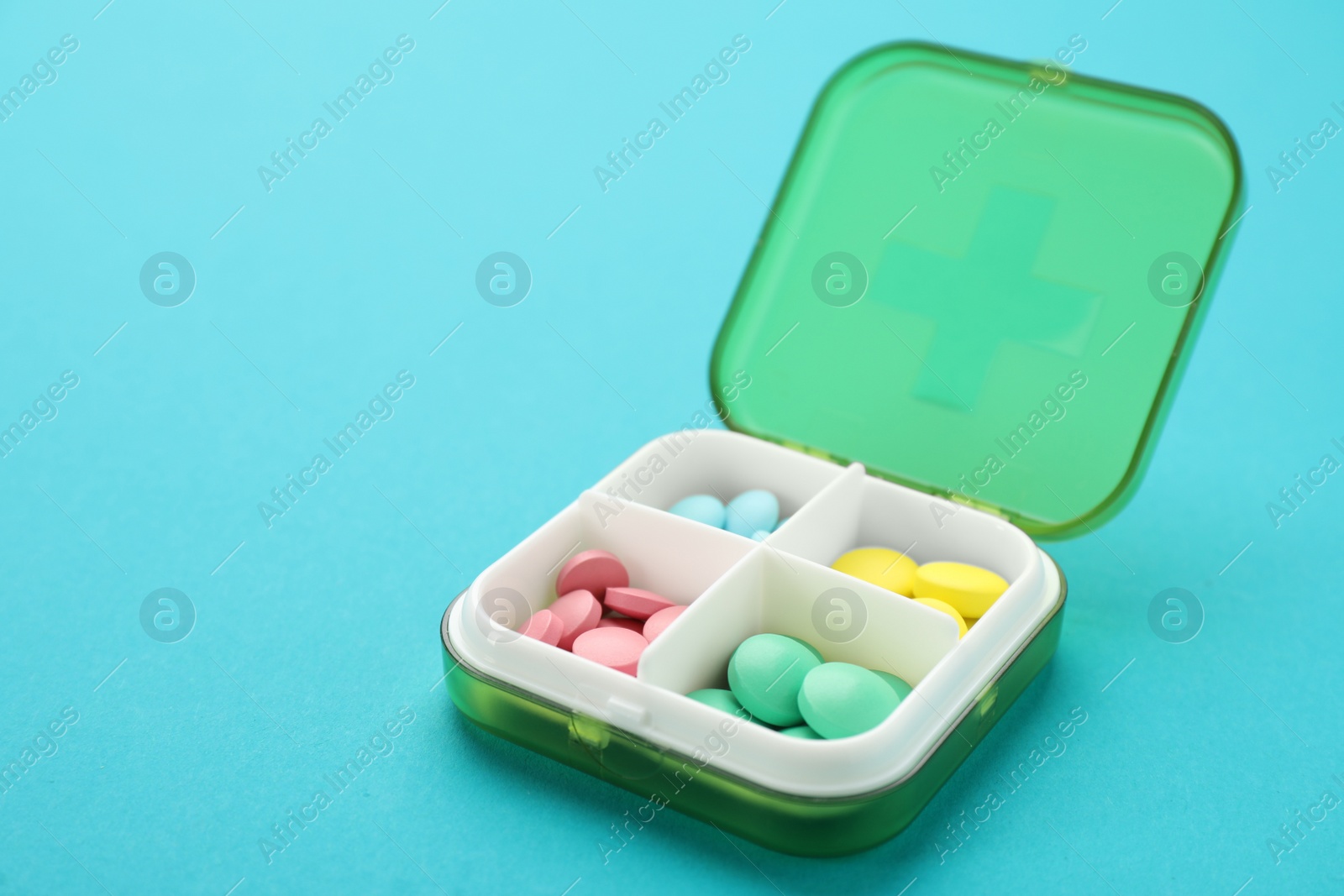 Plastic box with different pills on light blue background Photo of Plastic box with different pills on light blue background