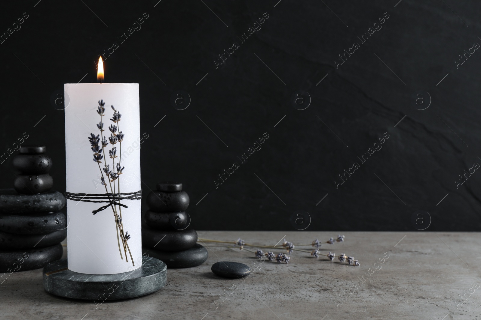 Photo of Burning candle with lavender and spa stones on grey table. Space for text