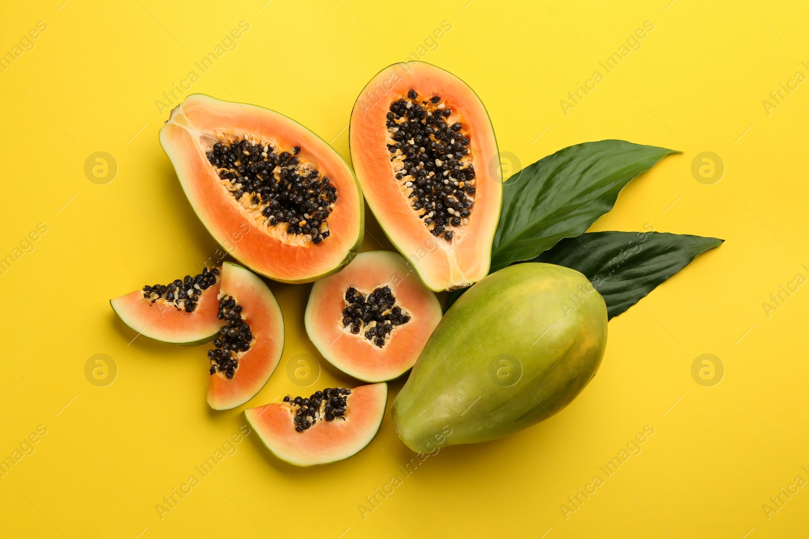 Fresh ripe papaya fruits with green leaves on yellow background, flat lay Photo of Fresh ripe papaya fruits with green leaves on yellow background, flat lay