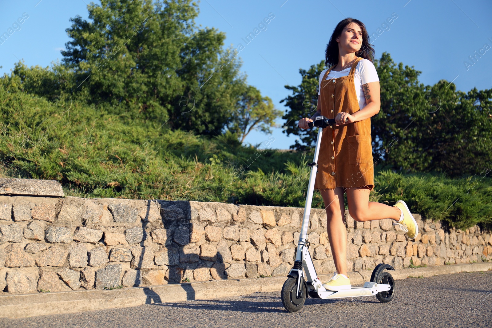 Young woman riding kick scooter along city street Photo of Young woman riding kick scooter along city street