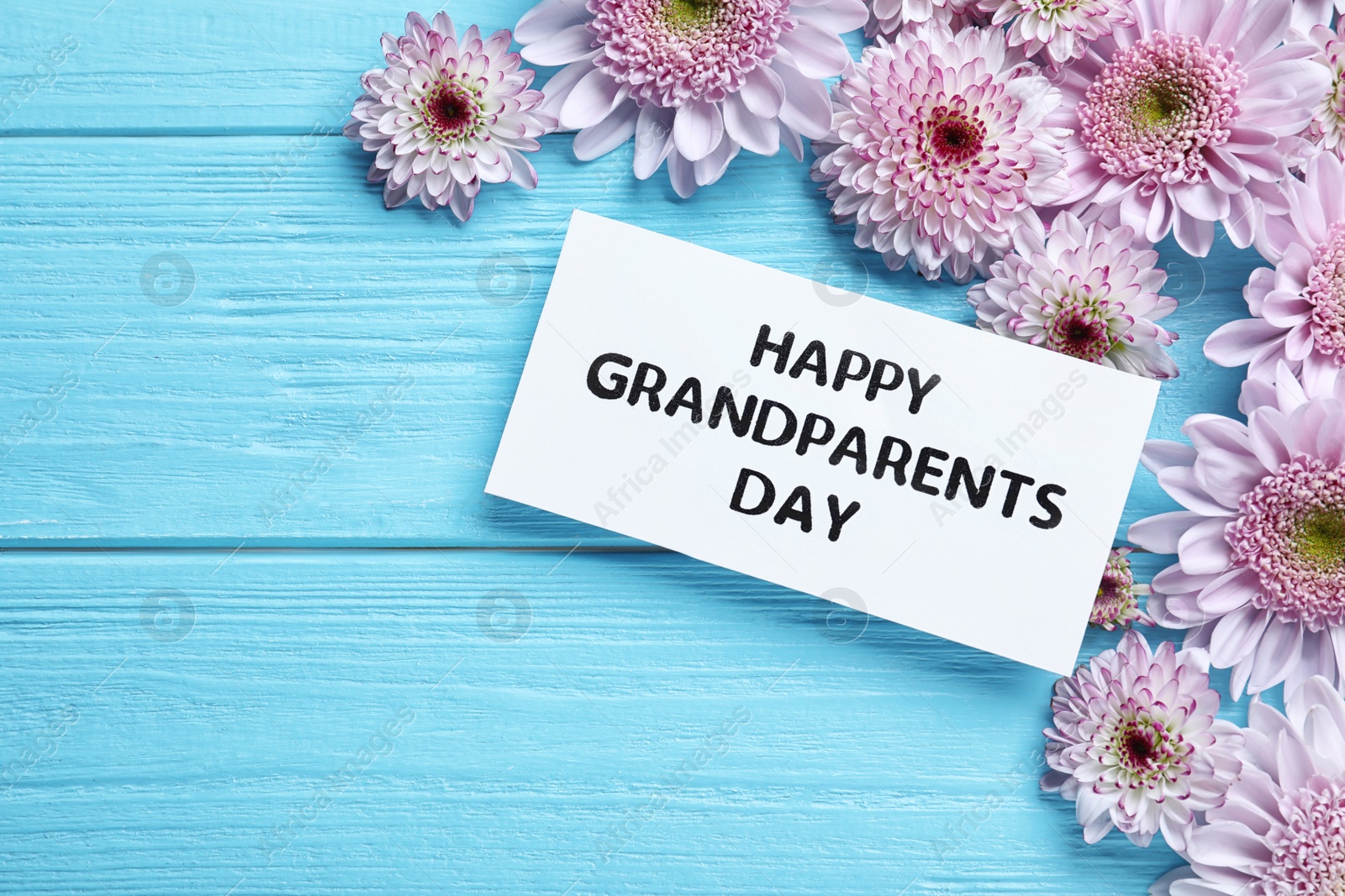 Beautiful flowers and card with phrase Happy Grandparents Day on light blue wooden background, flat lay. Space for text Photo of Beautiful flowers and card with phrase Happy Grandparents Day on light blue wooden background, flat lay. Space for text