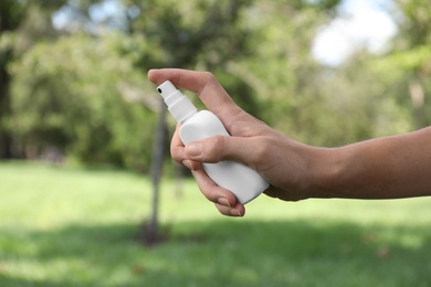 Woman with bottle of insect repellent spray outdoors, closeup Photo of Woman with bottle of insect repellent spray outdoors, closeup