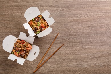 Boxes of wok noodles with seafood and chopsticks on wooden table, flat lay. Space for text Photo of Boxes of wok noodles with seafood and chopsticks on wooden table, flat lay. Space for text
