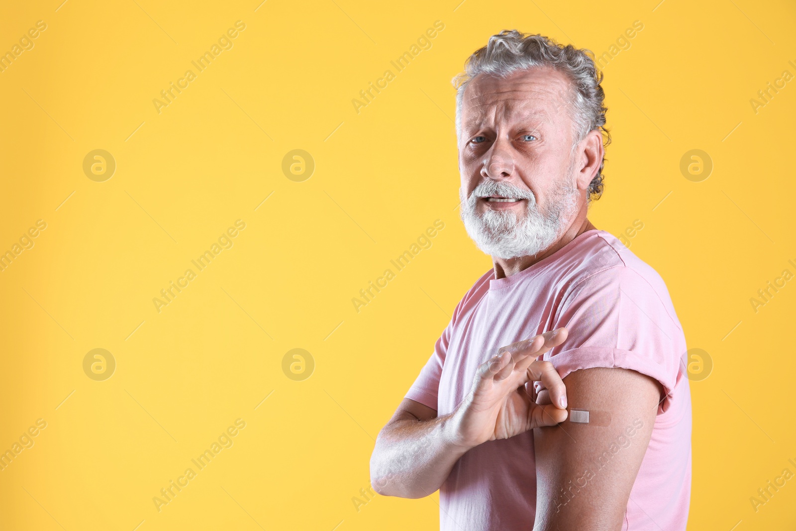 Cheerful senior man showing arm with bandage after vaccination on yellow background. Space for text Photo of Cheerful senior man showing arm with bandage after vaccination on yellow background. Space for text