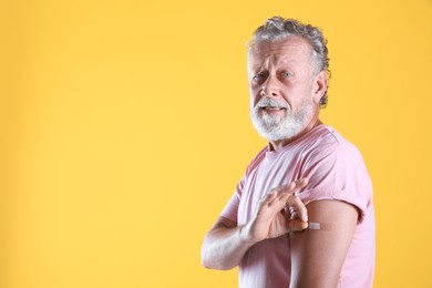 Cheerful senior man showing arm with bandage after vaccination on yellow background. Space for text Photo of Cheerful senior man showing arm with bandage after vaccination on yellow background. Space for text