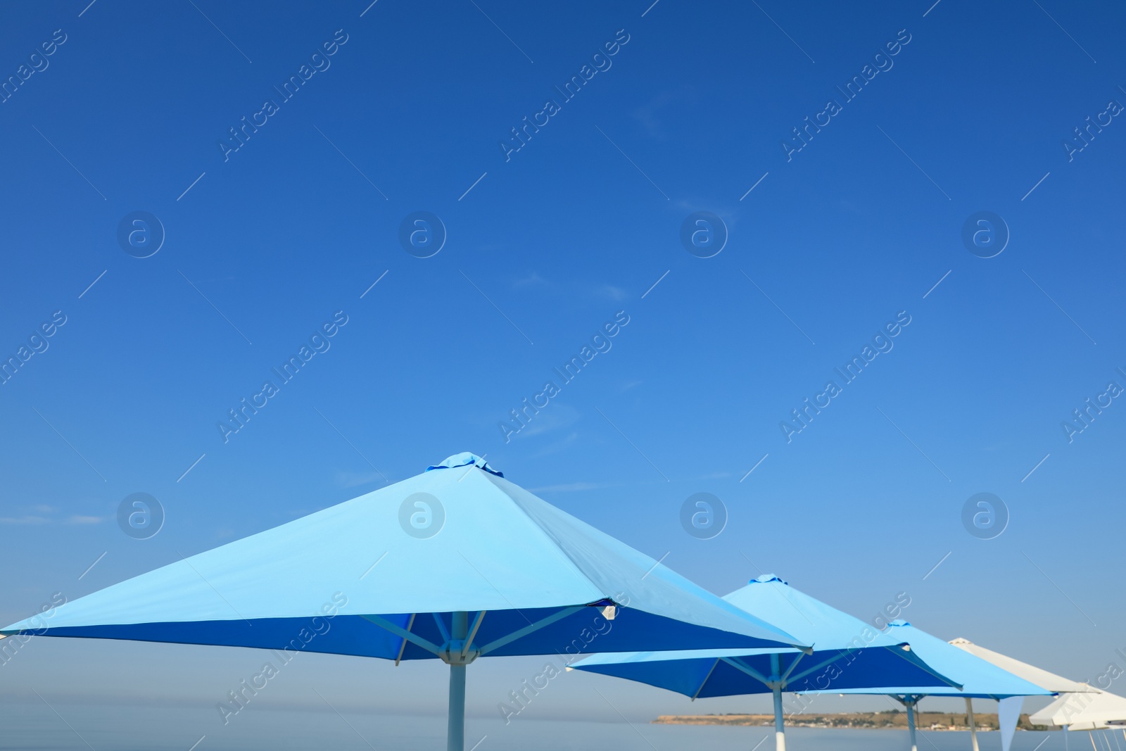 Bright beach umbrellas against blue sky on sunny day Photo of Bright beach umbrellas against blue sky on sunny day