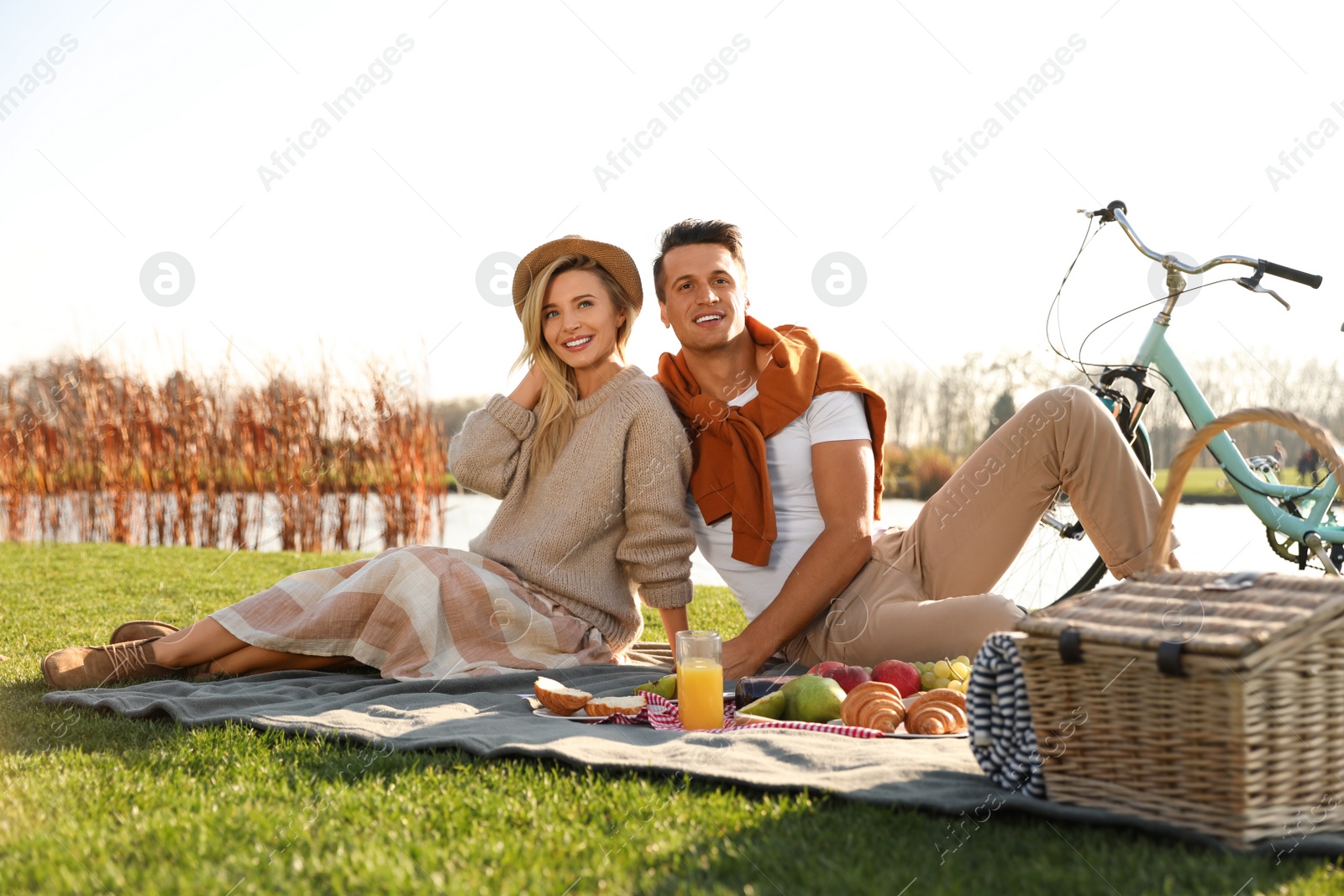 Happy young couple having picnic near lake on sunny day Photo of Happy young couple having picnic near lake on sunny day
