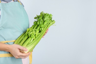 Woman holding fresh green celery on light background, closeup. Space for text Photo of Woman holding fresh green celery on light background, closeup. Space for text