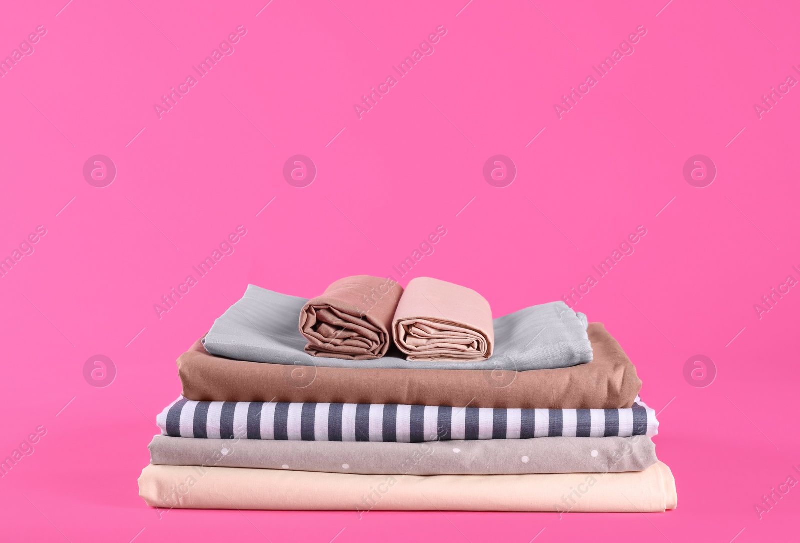 Stack of clean bed sheets on pink background. Space for text Photo of Stack of clean bed sheets on pink background. Space for text