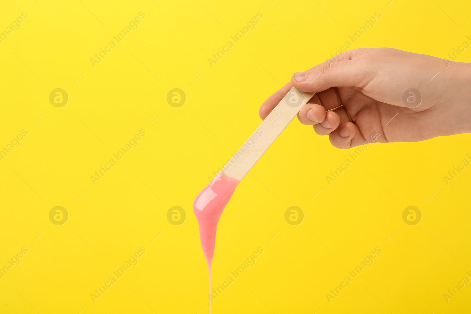Woman holding spatula with hot depilatory wax on yellow background, closeup Photo of Woman holding spatula with hot depilatory wax on yellow background, closeup