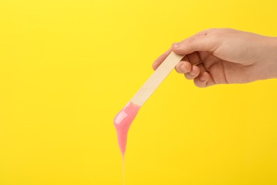 Woman holding spatula with hot depilatory wax on yellow background, closeup Photo of Woman holding spatula with hot depilatory wax on yellow background, closeup