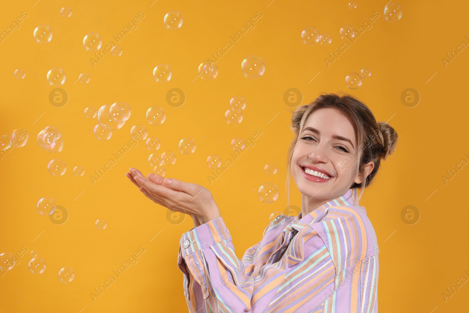 Young woman playing with soap bubbles on yellow background, space for text Photo of Young woman playing with soap bubbles on yellow background, space for text