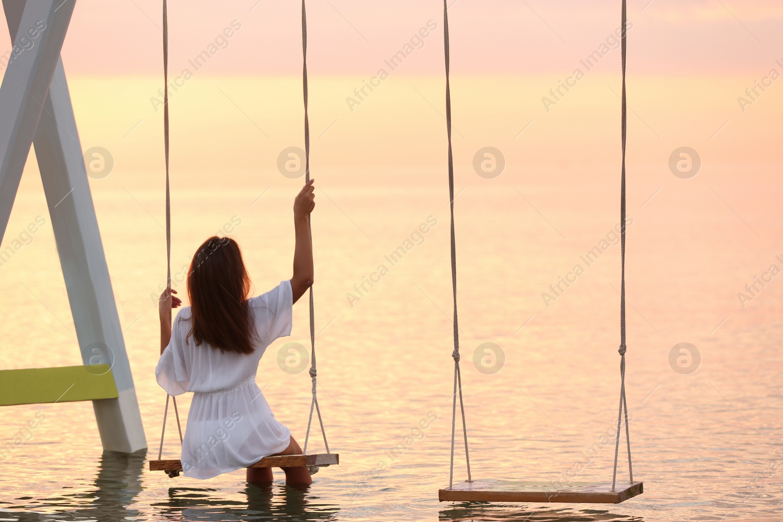 Young woman enjoying sunrise on swing over water Photo of Young woman enjoying sunrise on swing over water