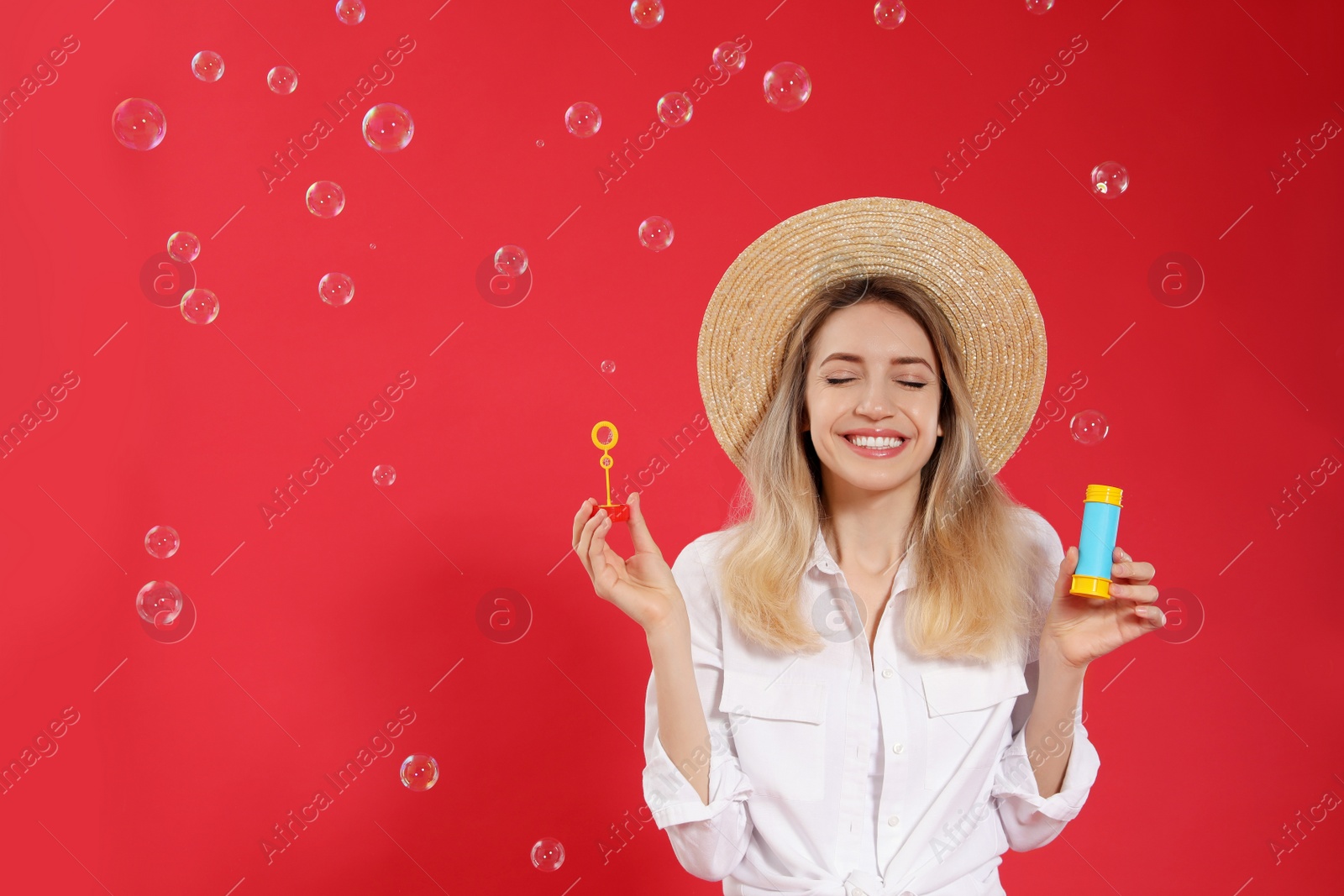 Young woman blowing soap bubbles on red background, space for text Photo of Young woman blowing soap bubbles on red background, space for text