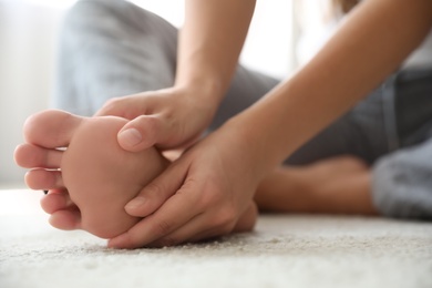 Young woman suffering from pain in foot on floor, closeup Photo of Young woman suffering from pain in foot on floor, closeup
