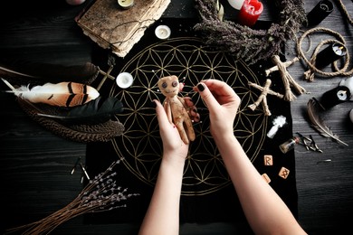 Photo of Woman stabbing voodoo doll with needle at table, closeup. Curse ceremony