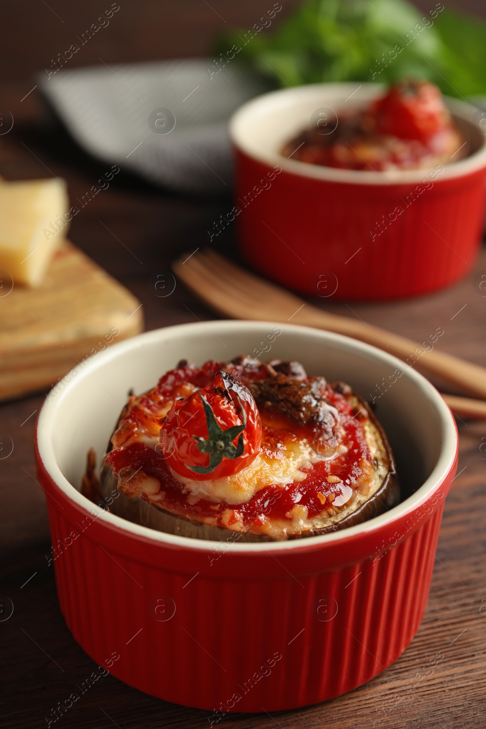 Baked eggplant with tomatoes and cheese in ramekin on wooden table, closeup Photo of Baked eggplant with tomatoes and cheese in ramekin on wooden table, closeup