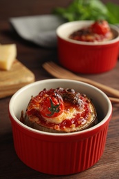 Baked eggplant with tomatoes and cheese in ramekin on wooden table, closeup Photo of Baked eggplant with tomatoes and cheese in ramekin on wooden table, closeup