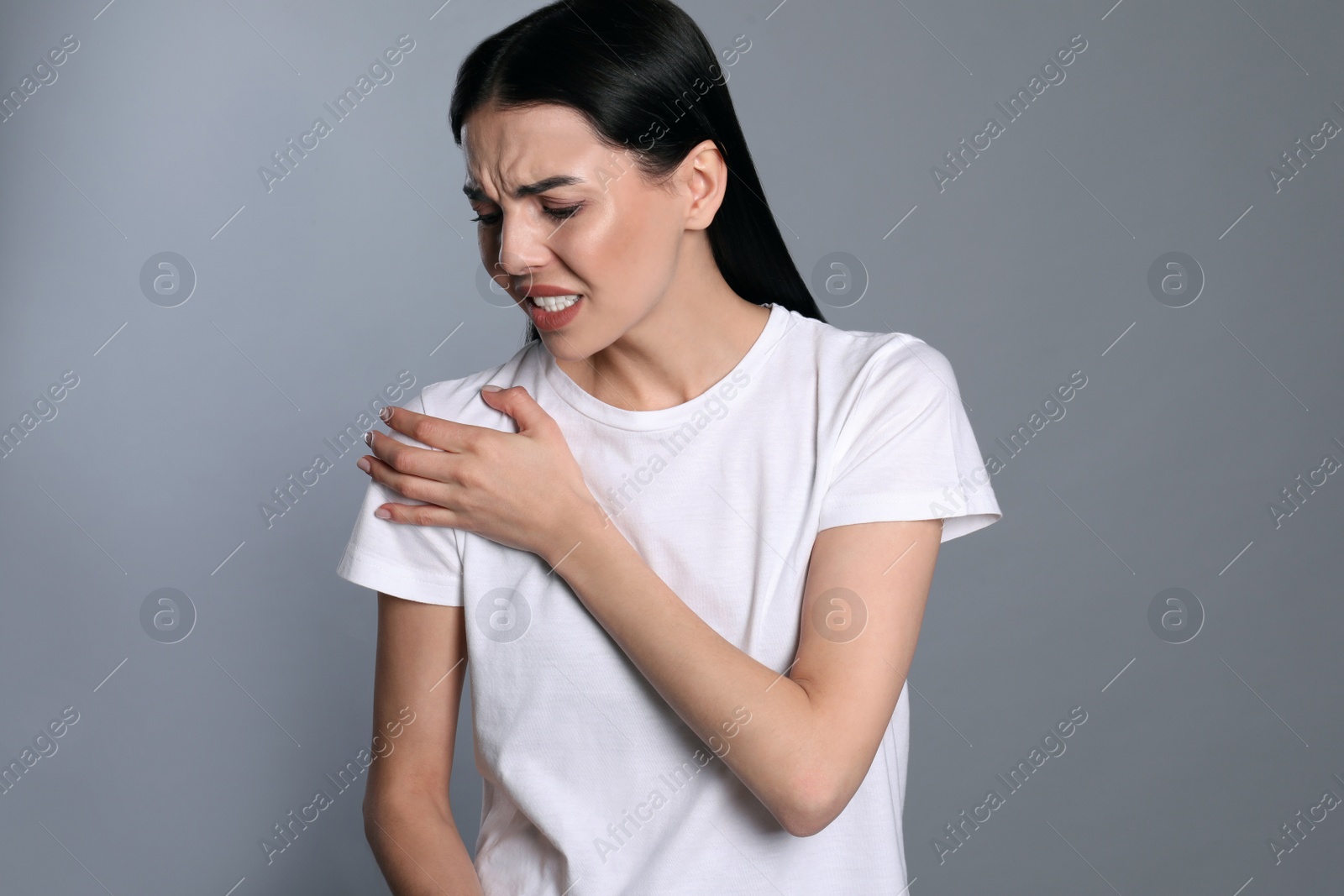Woman suffering from shoulder pain on grey background Photo of Woman suffering from shoulder pain on grey background