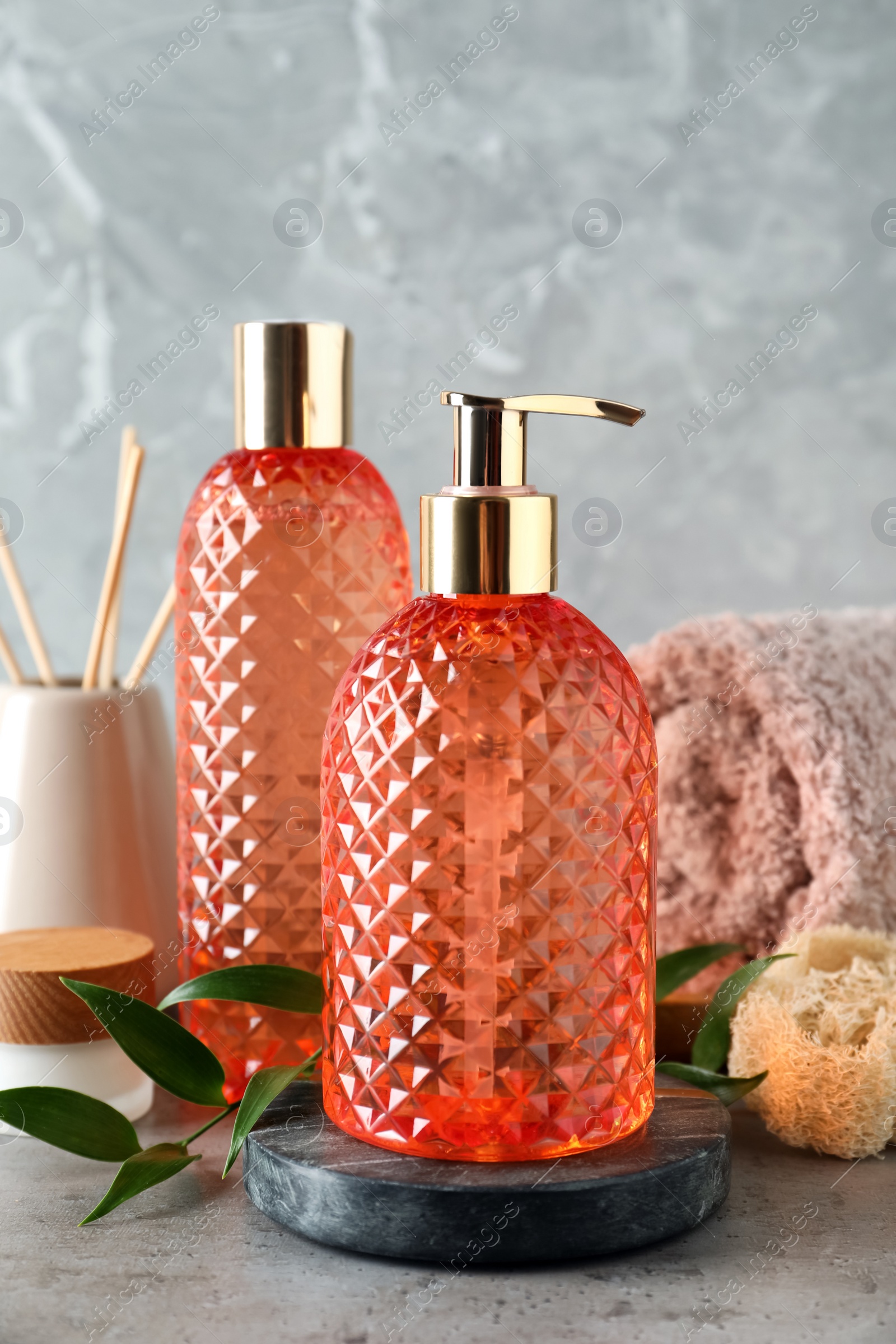 Stylish dispenser with liquid soap and other bathroom amenities on grey table Photo of Stylish dispenser with liquid soap and other bathroom amenities on grey table