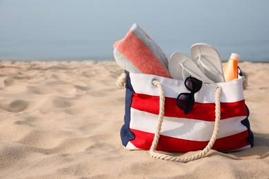 Beach bag with flip flops, towel, sunglasses and sunscreen on sandy seashore, space for text Photo of Beach bag with flip flops, towel, sunglasses and sunscreen on sandy seashore, space for text