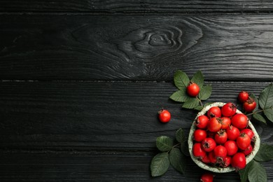 Ripe rose hip berries with green leaves on black wooden table, flat lay. Space for text Photo of Ripe rose hip berries with green leaves on black wooden table, flat lay. Space for text