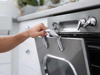 Photo of Man using modern oven in kitchen, closeup