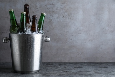 Metal bucket with bottles of beer and ice cubes on grey table, space for text Photo of Metal bucket with bottles of beer and ice cubes on grey table, space for text
