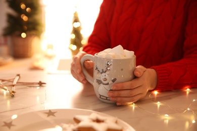Woman holding cup of hot drink with marshmallow indoors, closeup Photo of Woman holding cup of hot drink with marshmallow indoors, closeup