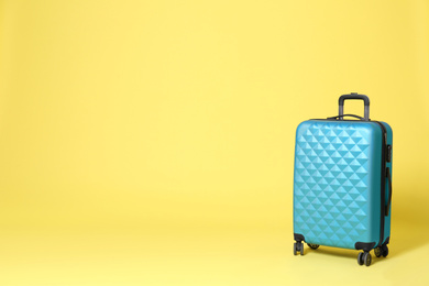 Photo of Stylish blue suitcase on yellow background. Space for text