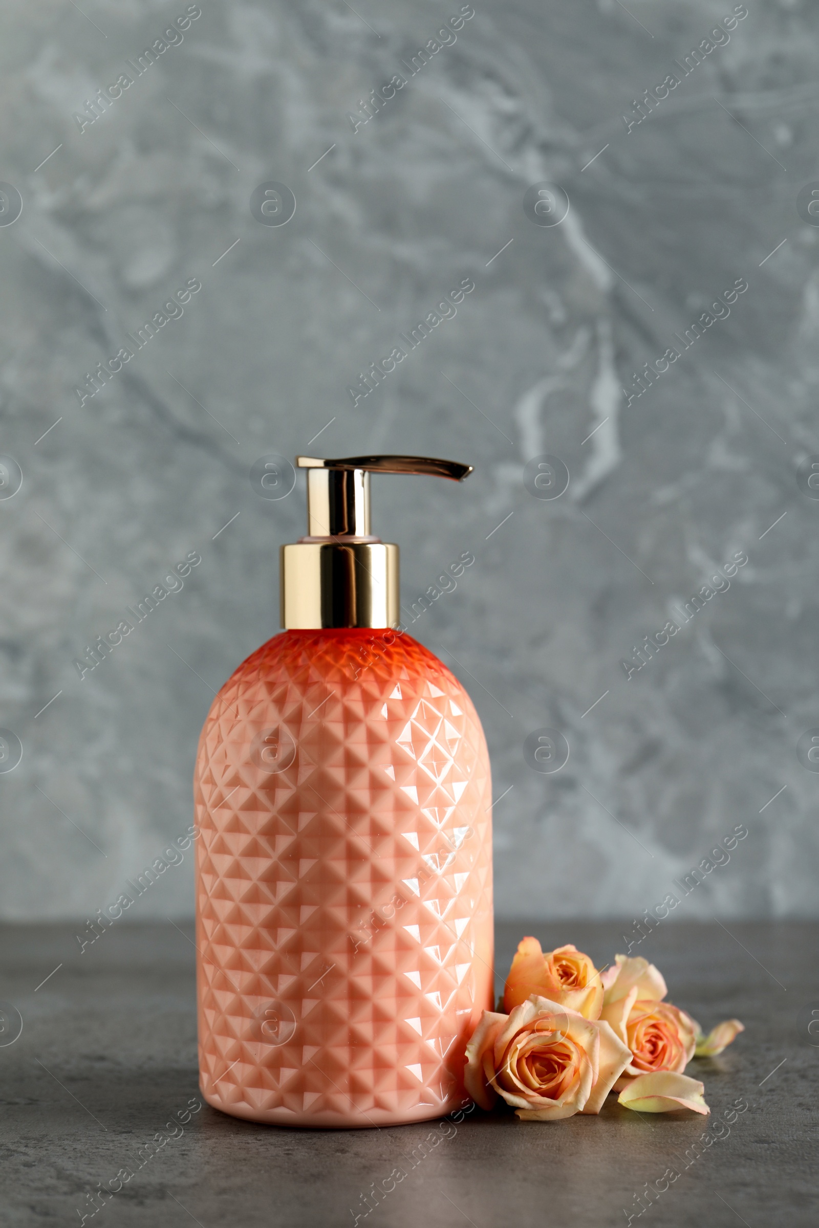 Stylish dispenser with liquid soap and beautiful flowers on grey table Photo of Stylish dispenser with liquid soap and beautiful flowers on grey table
