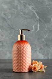 Stylish dispenser with liquid soap and beautiful flowers on grey table Photo of Stylish dispenser with liquid soap and beautiful flowers on grey table
