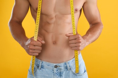 Shirtless man with slim body and measuring tape on yellow background, closeup Photo of Shirtless man with slim body and measuring tape on yellow background, closeup