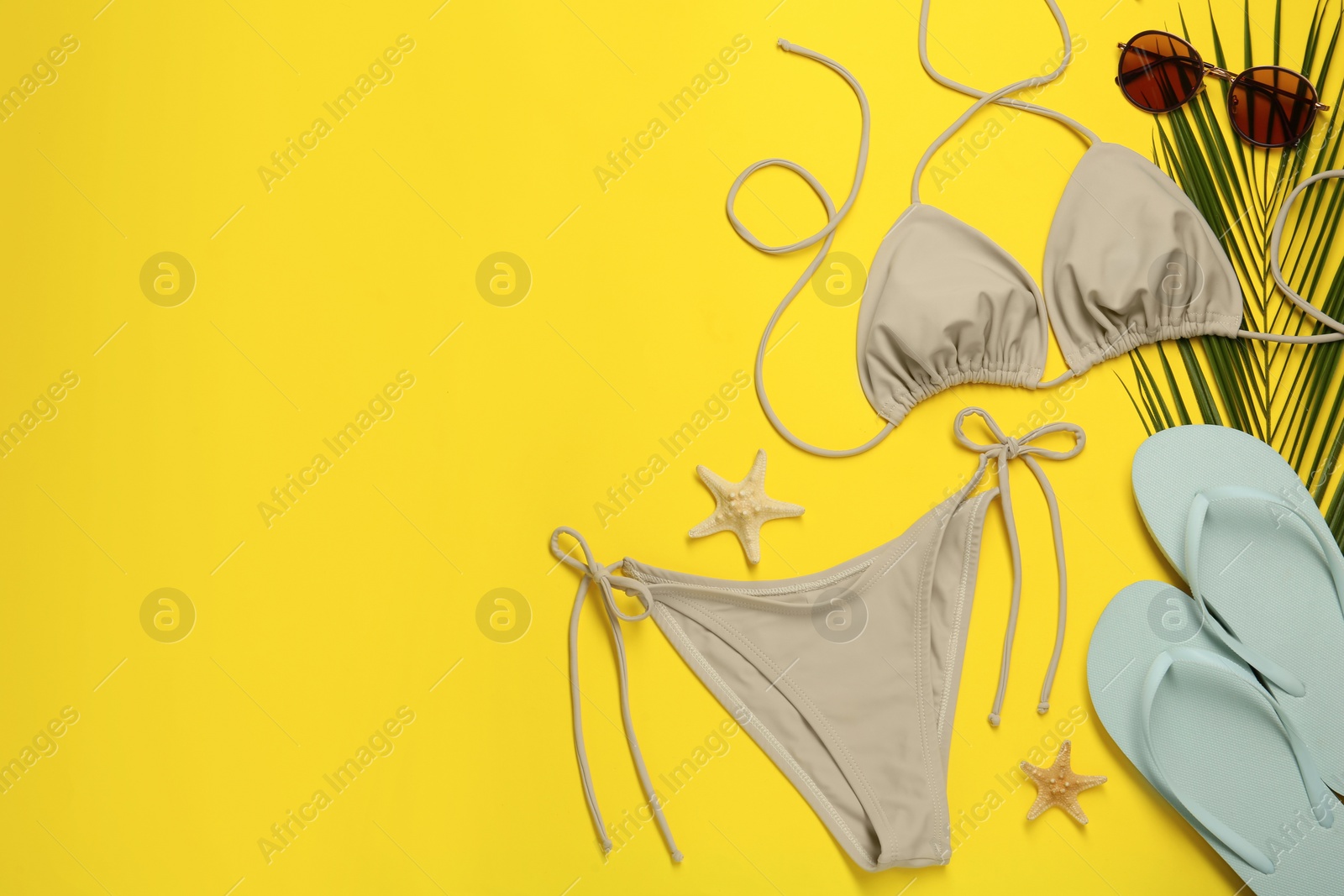 Stylish beige bikini and beach accessories on yellow background, flat lay. Space for text Photo of Stylish beige bikini and beach accessories on yellow background, flat lay. Space for text